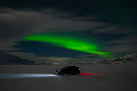 Car parked beneath green northern lights over the ice in Varanger