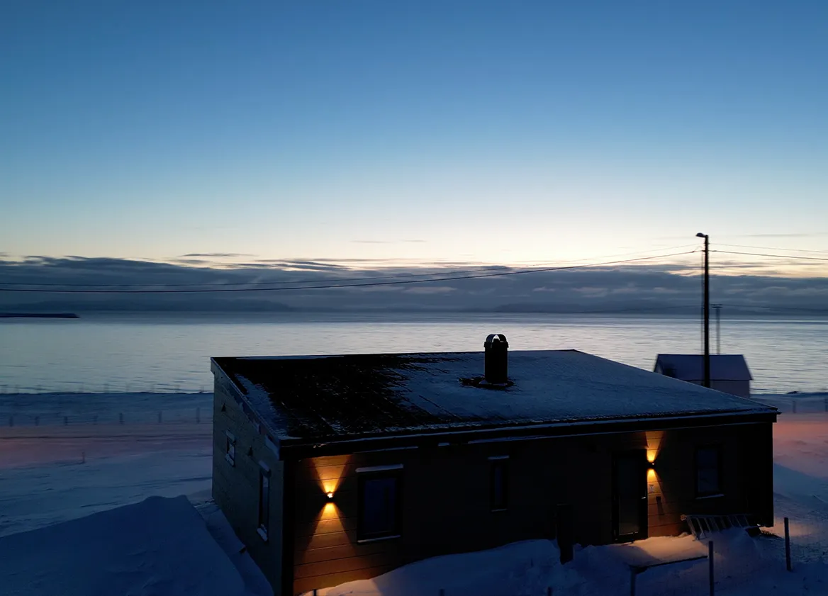 Vinterkveld ved Ekkerøy Lodge i skumring, med fjorden og fjellene i bakgrunnen