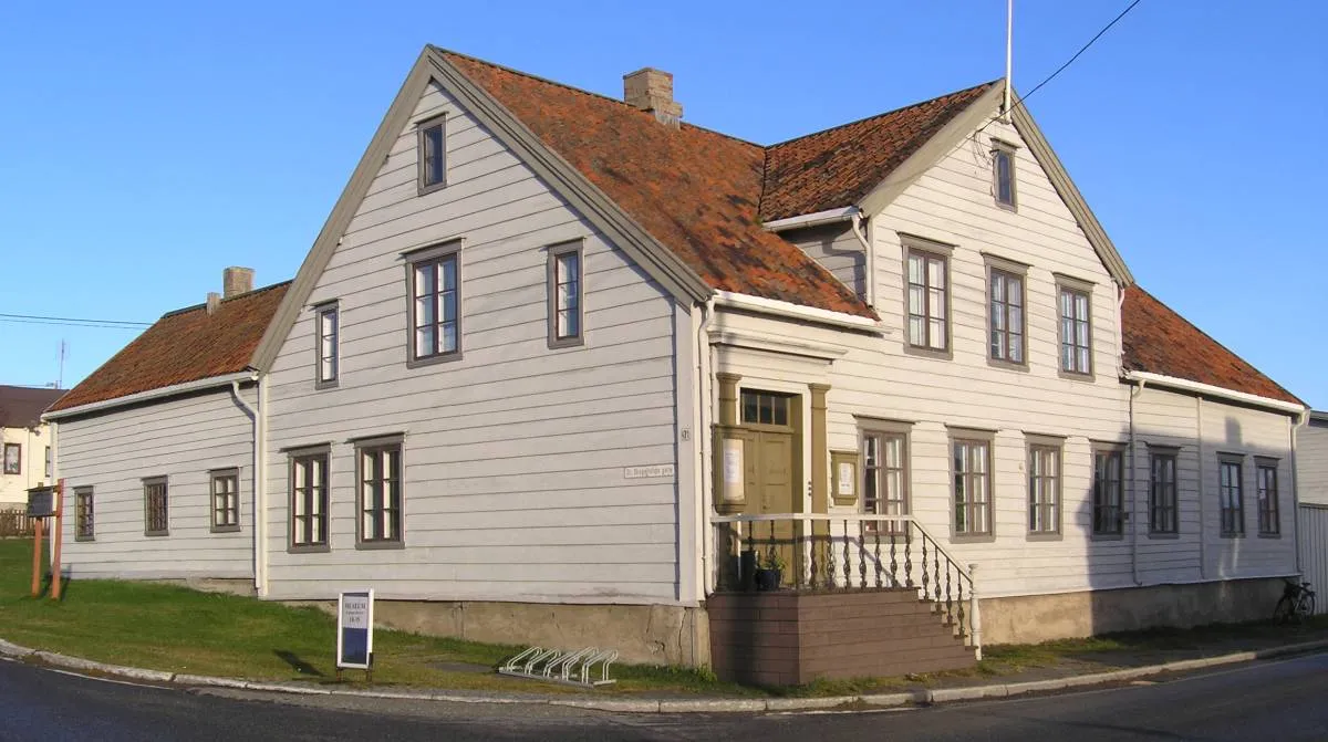 Esbensengårdens hvitmalte våningshus med rødt tegltak, fotografert en solfylt sommerdag fra gatehjørnet