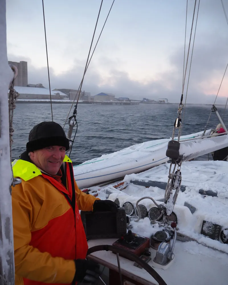 Skipper ved roret i snødekt båt på Varangerfjorden