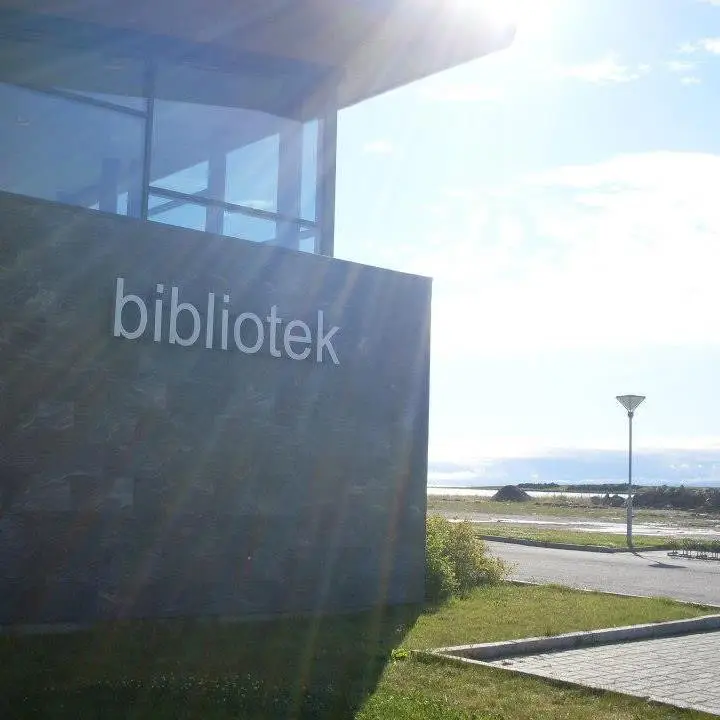 The entrance to Vadsø Library in sunshine, with the building’s slate panel and the metal letters “bibliotek”, the sea visible in the background