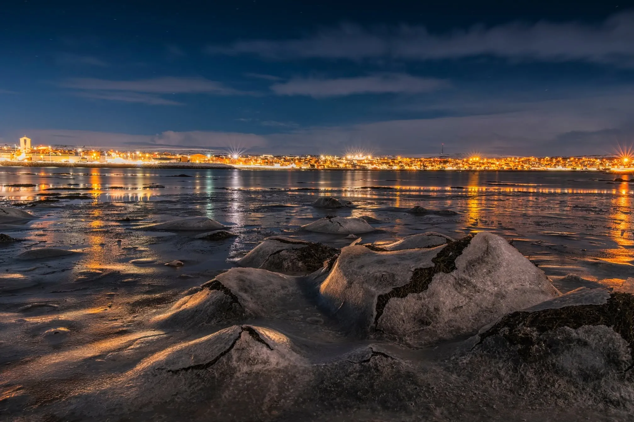 Vadsø seen from the sea on a winter evening, with the town lights reflected along the shore