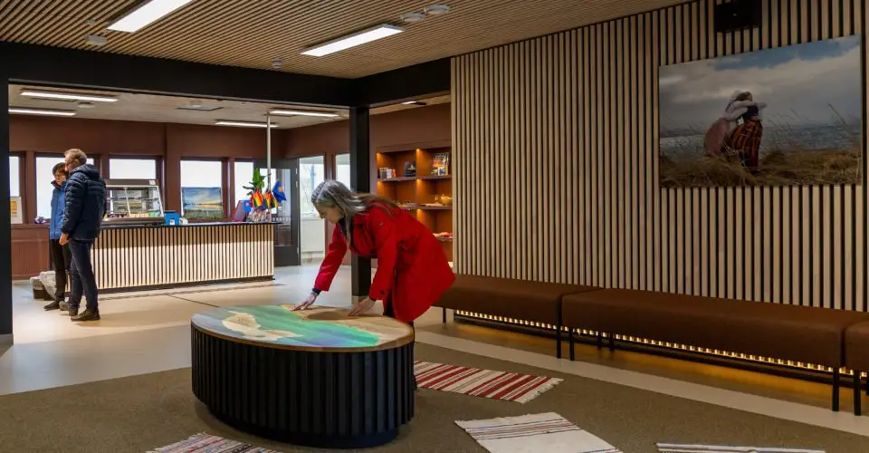 The foyer, with the museum shop in the background and a woman in a red jacket studying an illuminated relief model of the Varanger Peninsula