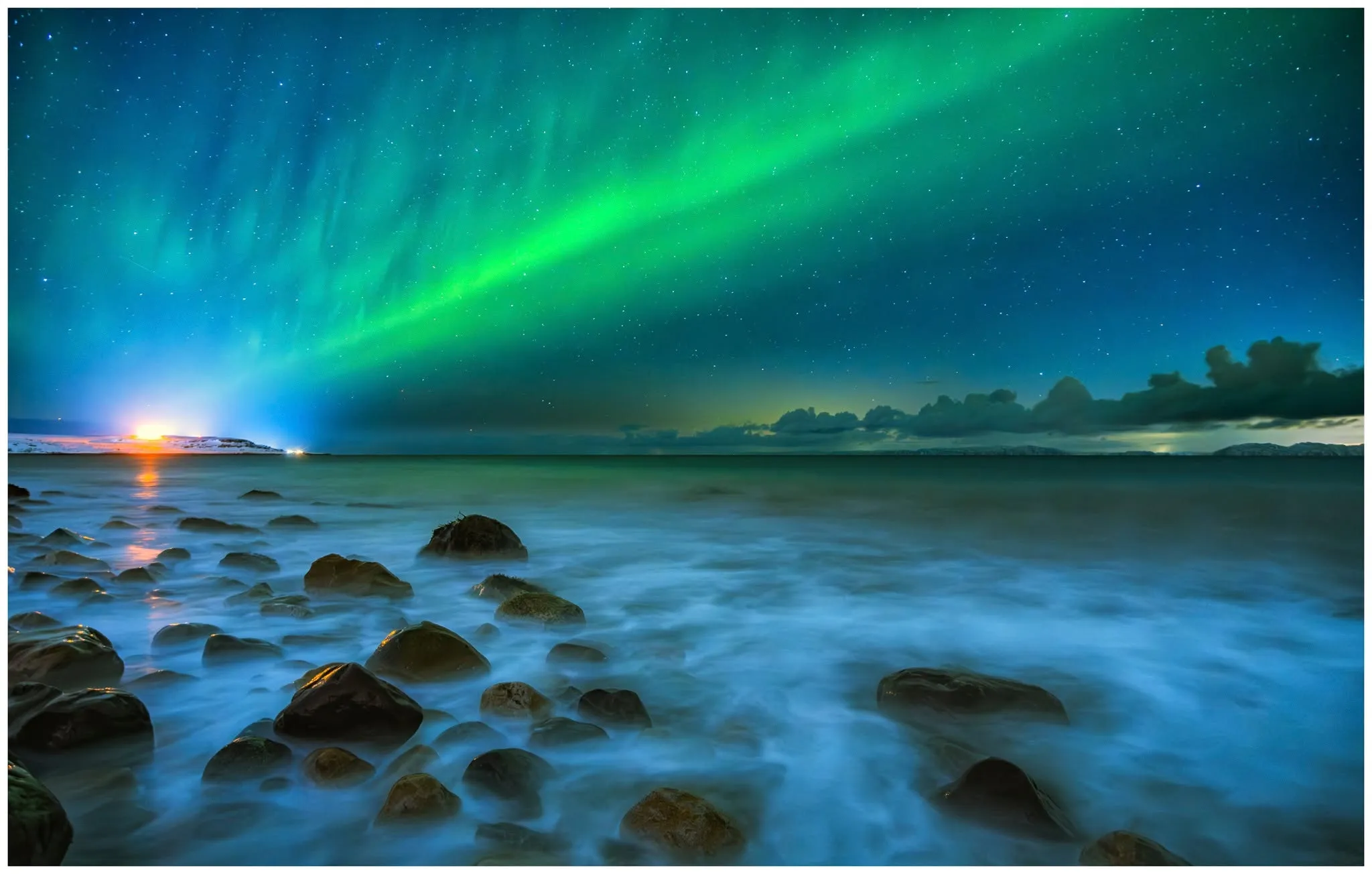 Nordlys over Varangerfjorden sett fra Vadsøya, med bølger mot steinstranden